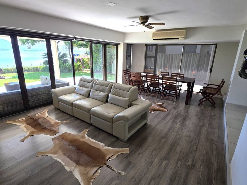 Spacious open-plan living and dining area featuring laminate flooring, ceiling fan, air conditioning, and large sliding glass doors opening to a garden view.