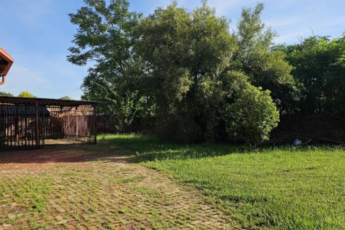 A spacious rear garden area featuring a paved section, established trees, and a covered outdoor structure, offering potential for landscaping and outdoor living.