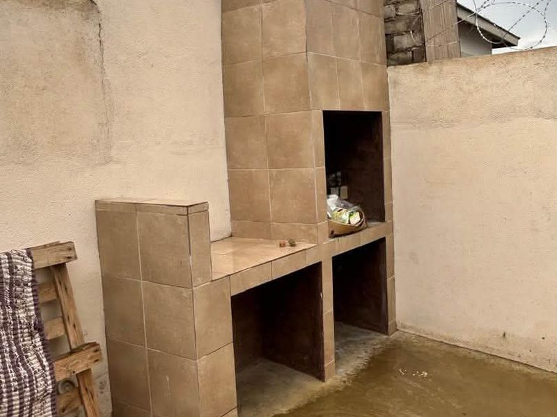 Outdoor patio area featuring a built-in tiled braai station, concrete flooring, and perimeter walling secured with razor wire.