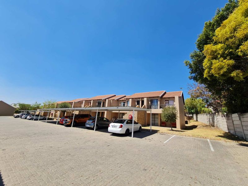 Exterior view of a residential apartment complex featuring covered parking bays, tiled roofing, and private balconies.