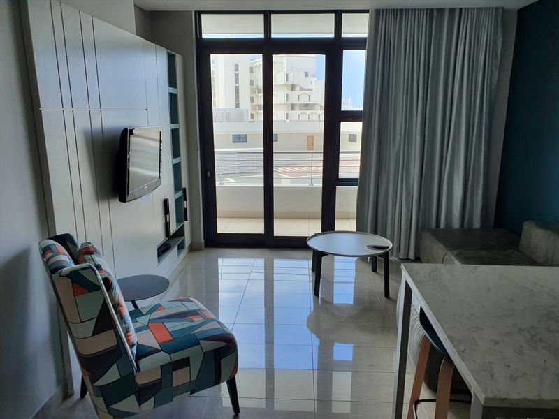 A modern living area featuring tiled flooring, a built-in media unit, and large sliding glass doors providing access to a balcony.