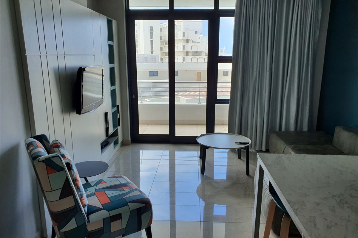 A modern living area featuring tiled flooring, a built-in media unit, and large sliding glass doors providing access to a balcony.