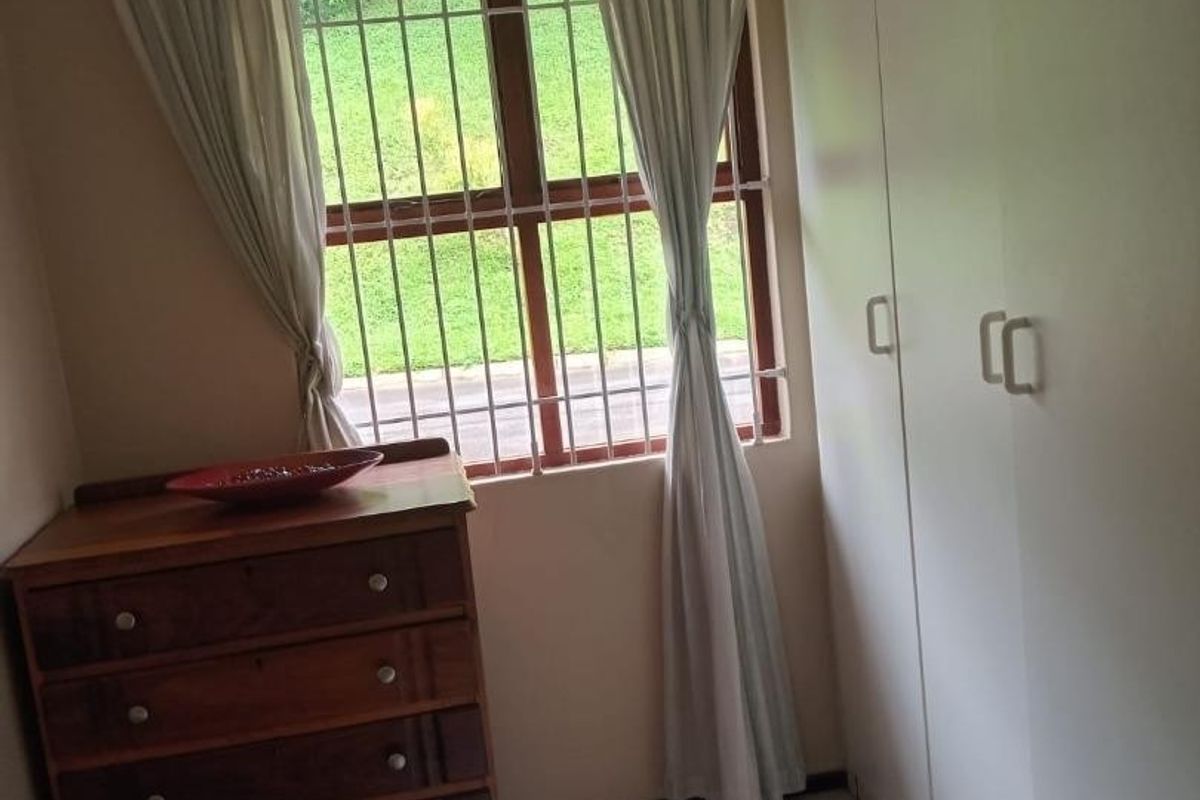 A bedroom featuring built-in cupboards, tiled flooring, and a window fitted with security bars, offering a functional and secure living space.