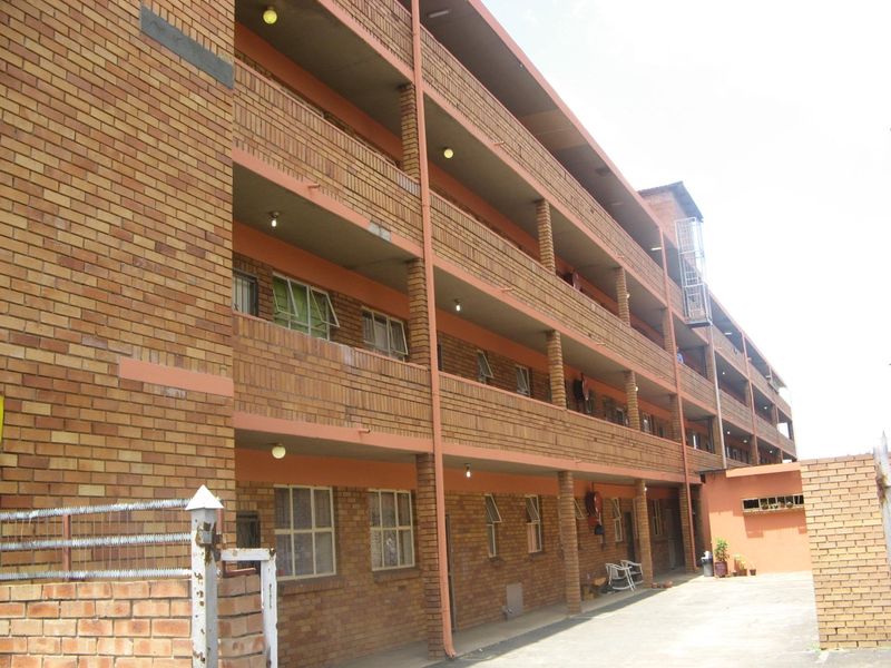 A multi-story apartment building featuring a face brick facade with external walkways and steel-framed windows.