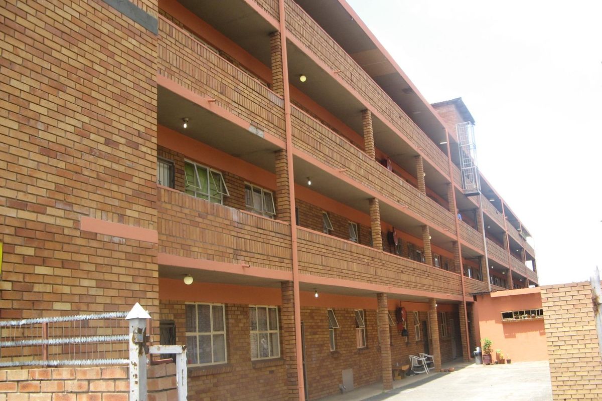 A multi-story apartment building featuring a face brick facade with external walkways and steel-framed windows.