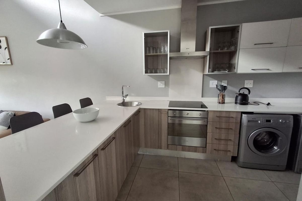 Modern kitchen featuring wood-finish cabinetry, white stone countertops, integrated appliances, and tiled flooring, offering a clean and functional cooking space.