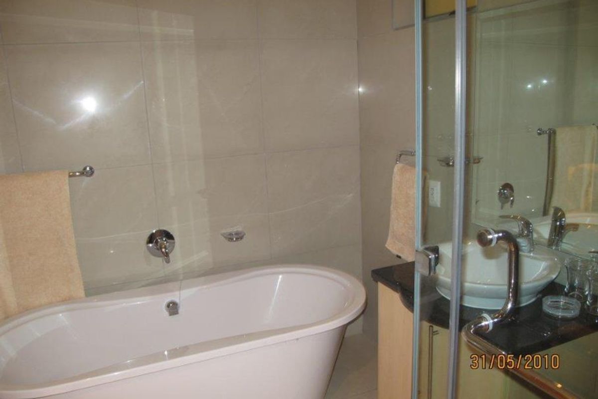 A bathroom featuring a freestanding bathtub, a vessel sink with a granite vanity top, and a glass-enclosed shower area with tiled walls.