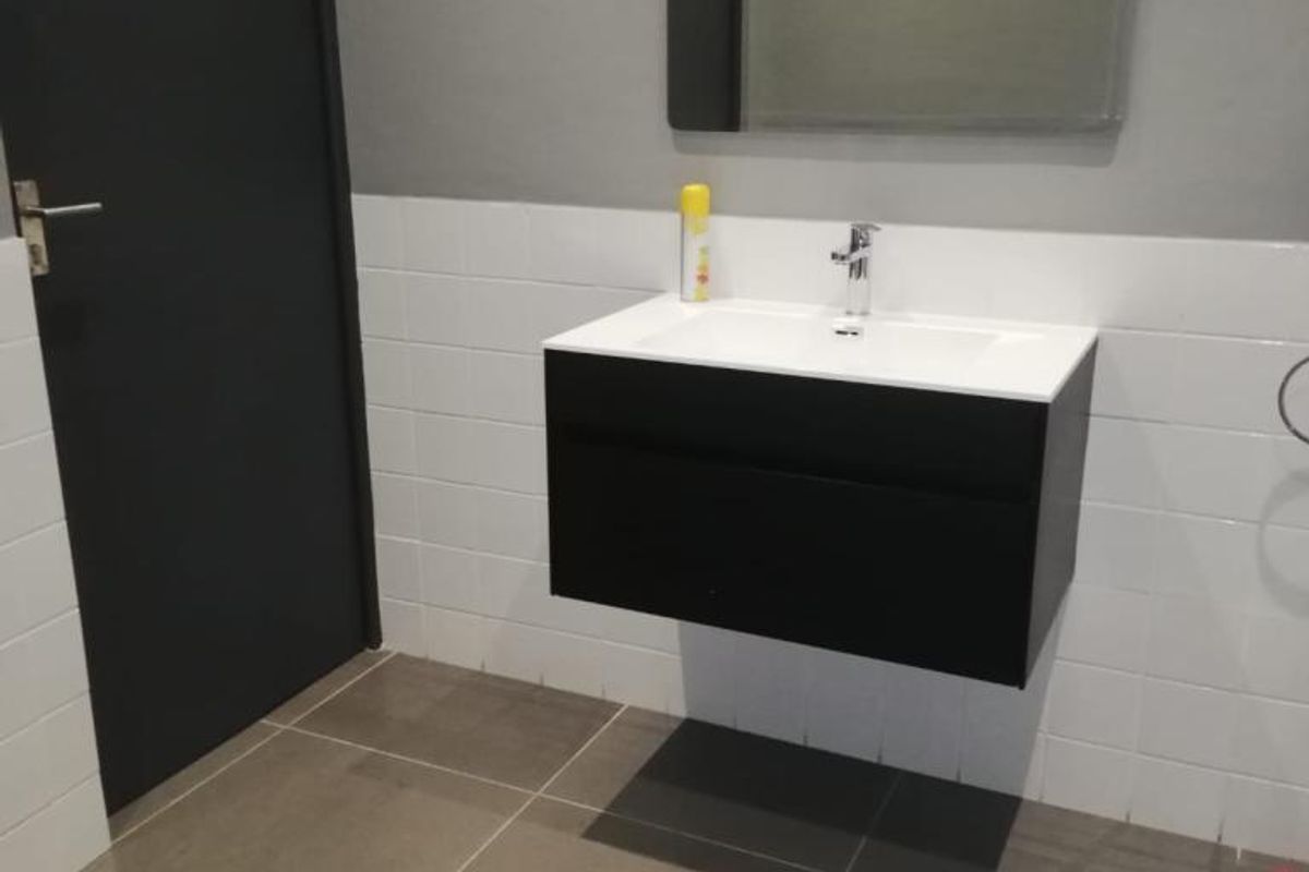 A modern, minimalist bathroom featuring a sleek wall-mounted vanity with an integrated basin, complemented by neutral wall and floor tiling.