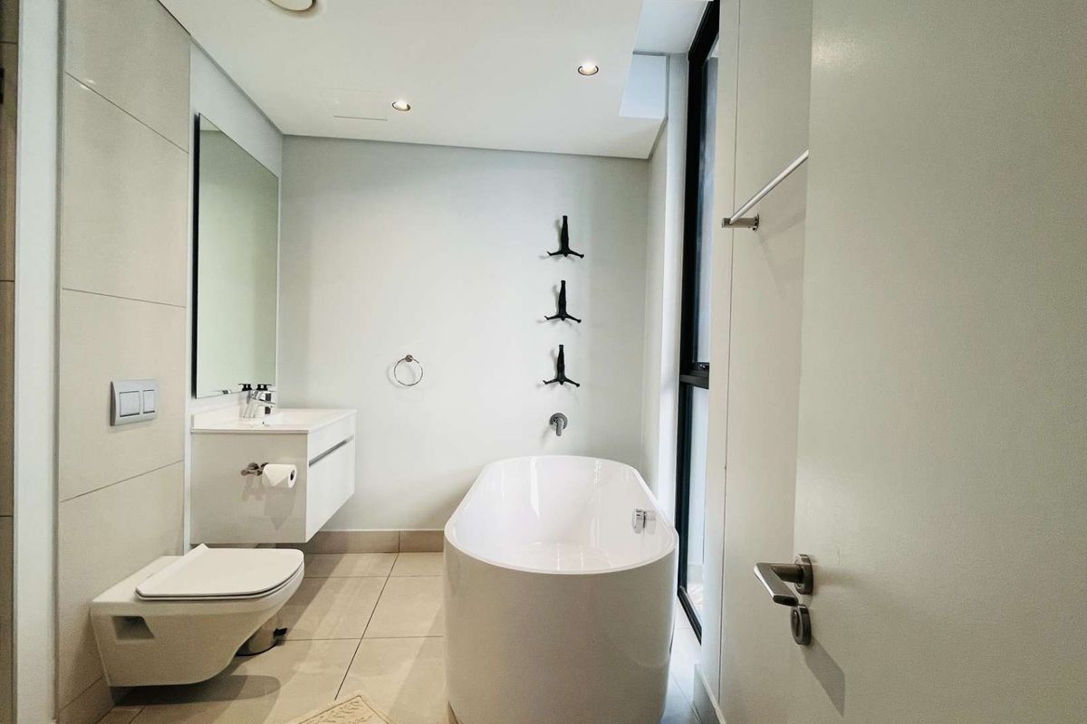 Modern bathroom featuring a freestanding bathtub, wall-mounted toilet, floating vanity with integrated basin, and large format floor tiles.