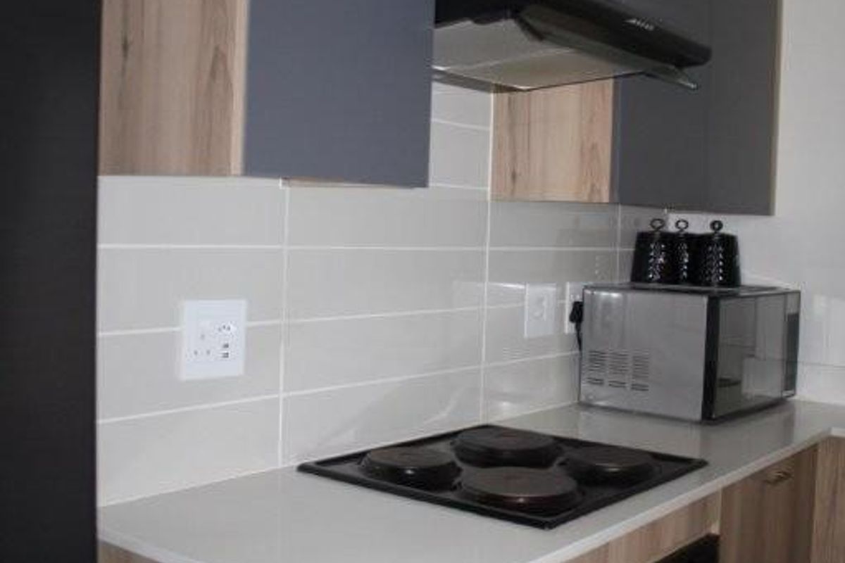 Modern kitchen featuring two-tone cabinetry, light stone countertops, subway tile backsplash, and integrated electric hob and oven.