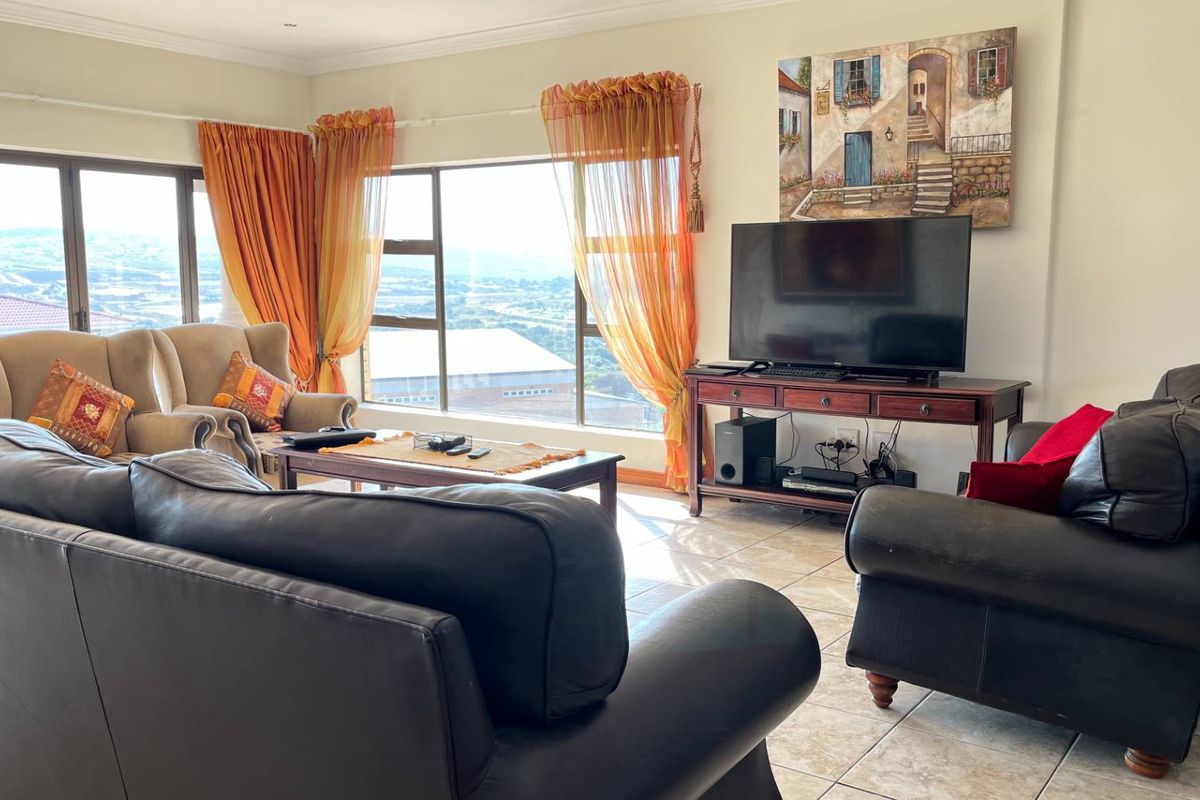 A spacious living room featuring large windows with expansive views, tiled flooring, and neutral wall finishes.