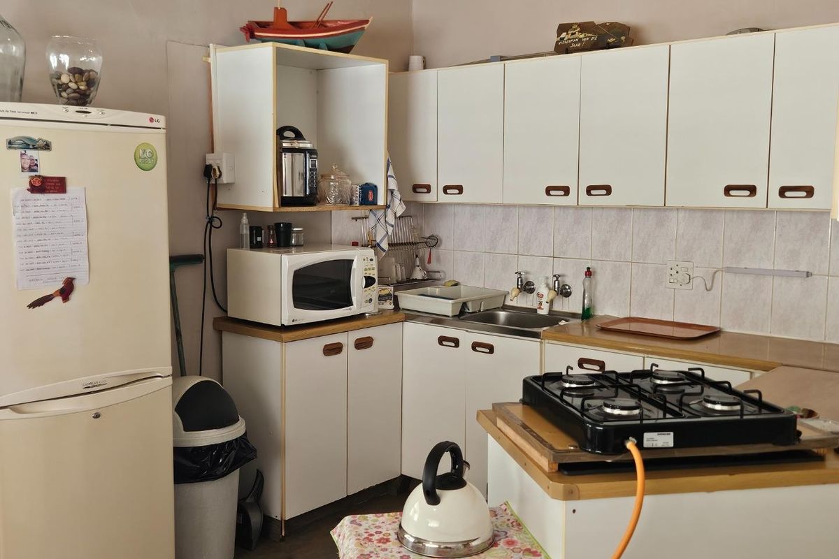 A compact kitchen featuring white cabinetry, tiled splashbacks, a stainless steel sink, and a portable gas hob setup.