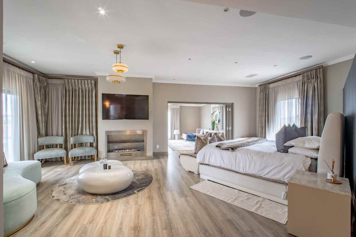 Spacious primary bedroom suite featuring wood-look flooring, a built-in fireplace, recessed lighting, and direct access to an adjoining sitting area.