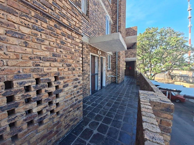 Exterior walkway featuring face brick walls, a decorative breeze block section, and tiled flooring, providing access to the apartment units.