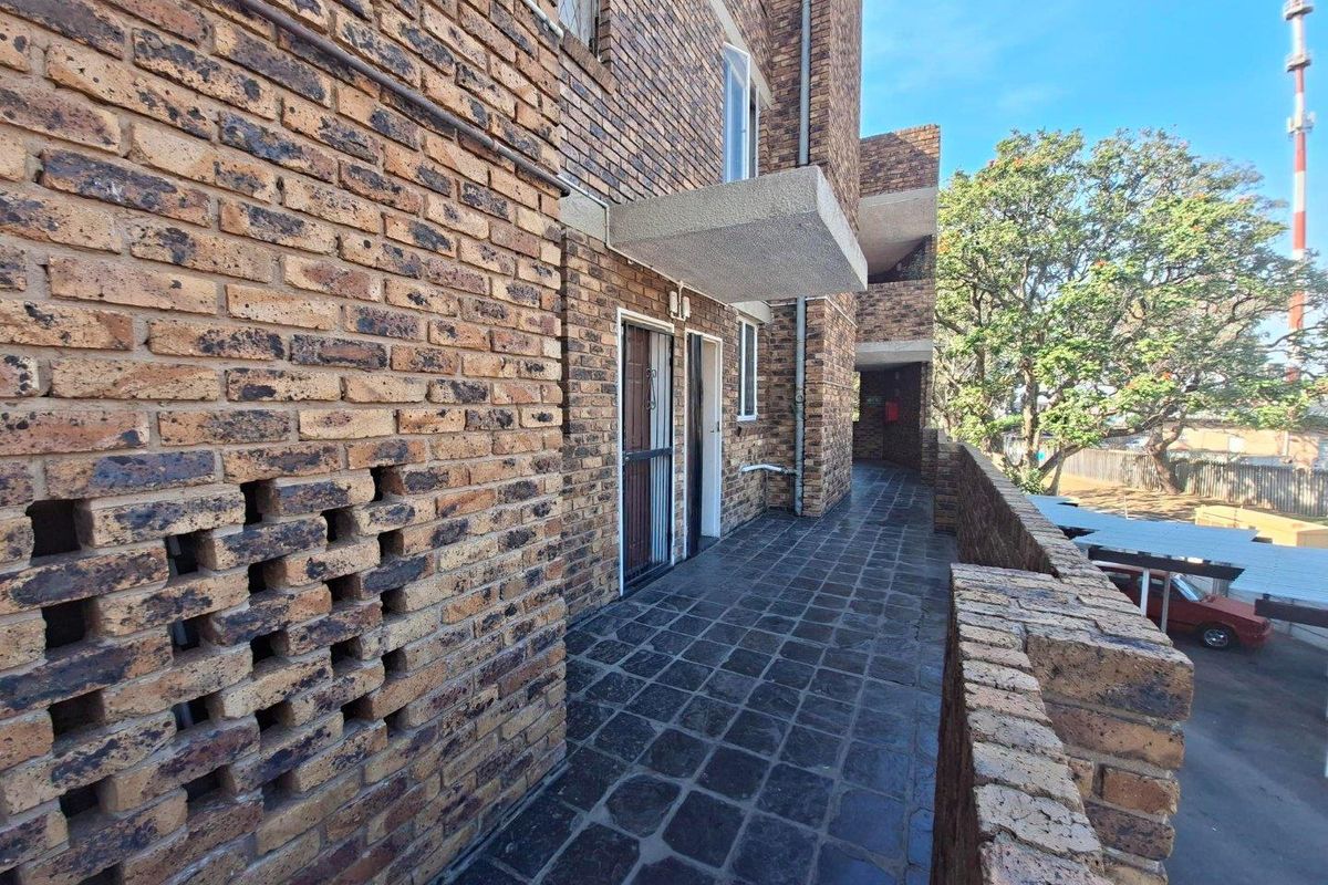 Exterior walkway featuring face brick walls, a decorative breeze block section, and tiled flooring, providing access to the apartment units.