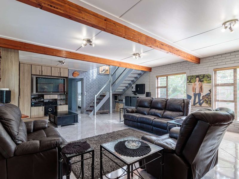 Spacious living room featuring exposed timber ceiling beams, painted brick walls, tiled flooring, and a built-in entertainment unit with an integrated staircase.