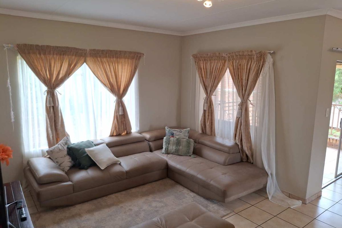 A bright and spacious living room featuring neutral wall tones, tiled flooring, and large windows that provide ample natural light.