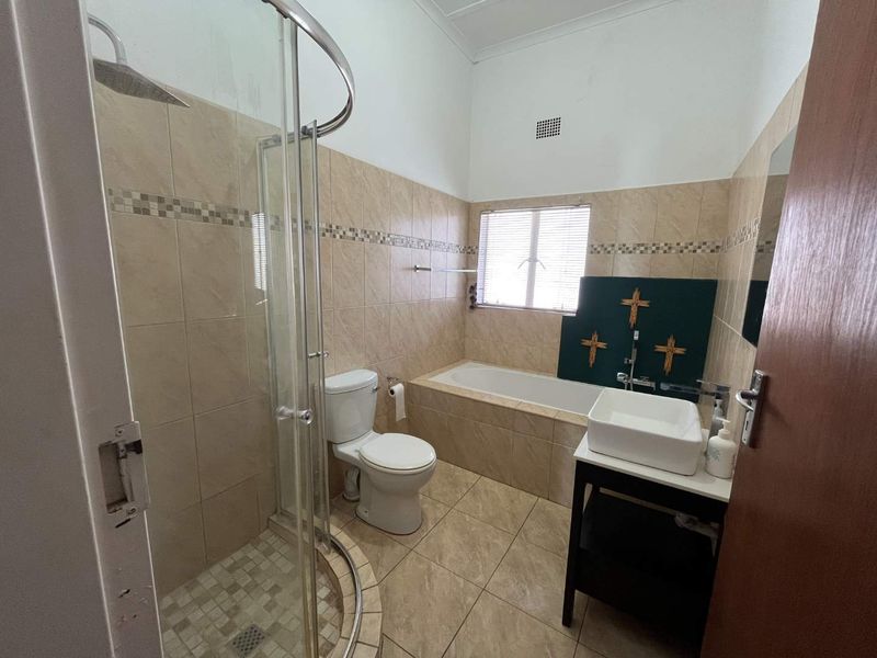 A functional bathroom featuring a glass shower enclosure, a built-in bathtub, a toilet, and a vessel sink with tiled finishes throughout.