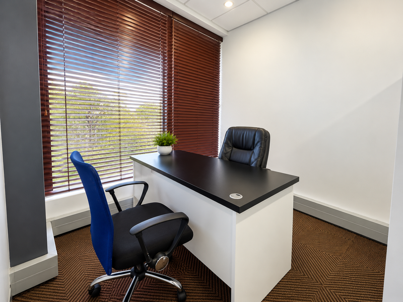 A professional office space featuring carpeted flooring, recessed ceiling lights, and large windows fitted with venetian blinds.