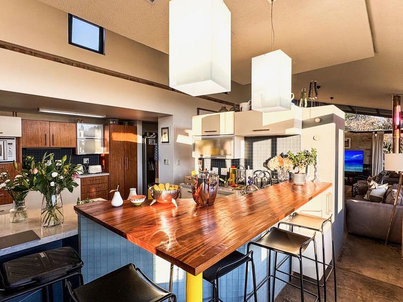 An open-plan kitchen and living area featuring a prominent wooden breakfast bar, modern cabinetry, and stylish pendant lighting with a bright, airy atmosphere.