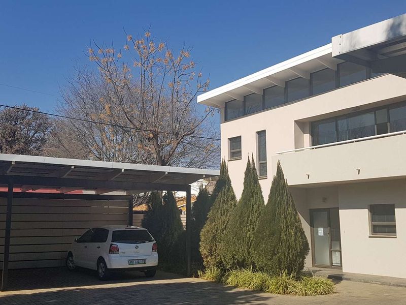 Front exterior view of a modern office building featuring a paved driveway, covered carport, and a balcony with clean architectural lines.