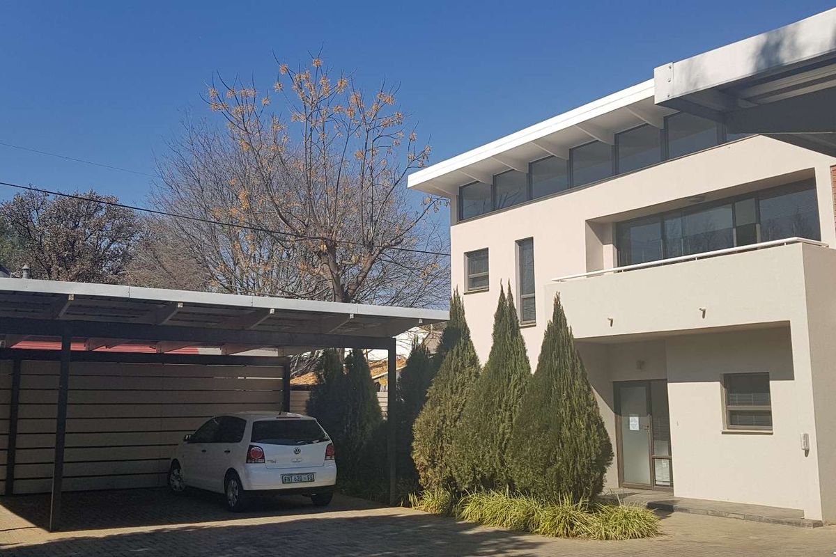 Front exterior view of a modern office building featuring a paved driveway, covered carport, and a balcony with clean architectural lines.