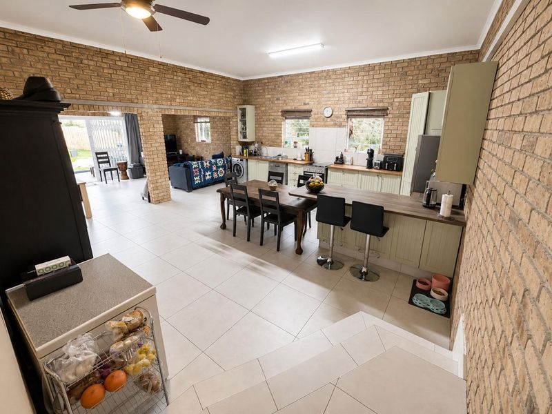Spacious open-plan living and kitchen area featuring exposed brick walls, tiled flooring, and a functional kitchen with a central island and breakfast bar.