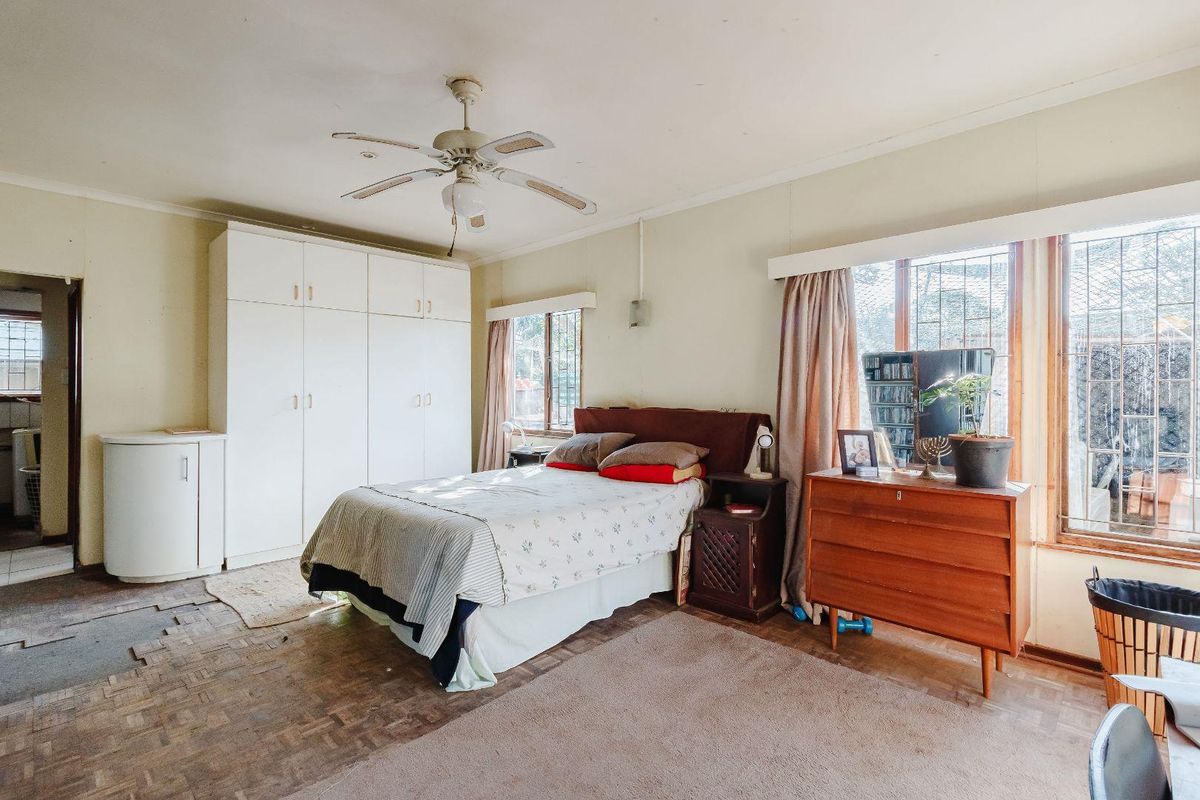 Spacious bedroom featuring built-in cupboards, a ceiling fan, and security bars on the windows. The room requires flooring repairs and cosmetic updates.
