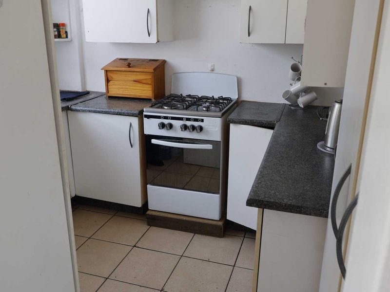 Compact kitchen featuring white cabinetry, dark laminate countertops, and a freestanding gas stove with tiled flooring.