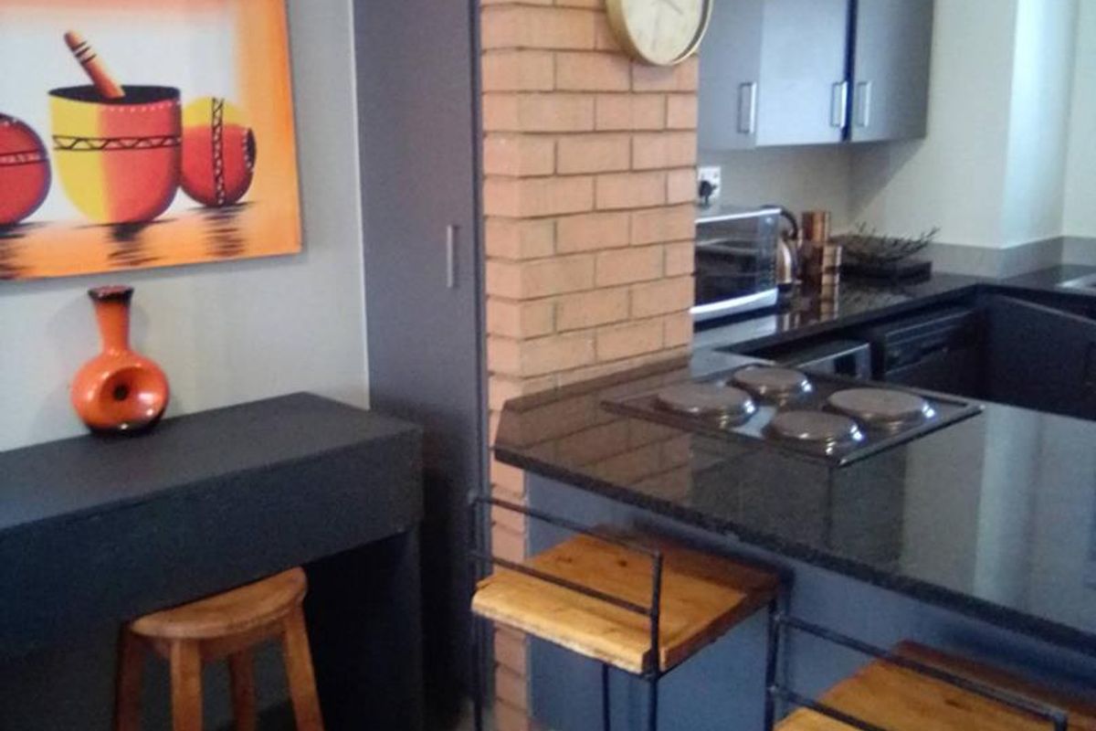 Modern kitchen featuring dark grey cabinetry, granite countertops, a built-in electric hob, and a distinctive exposed brick feature pillar.