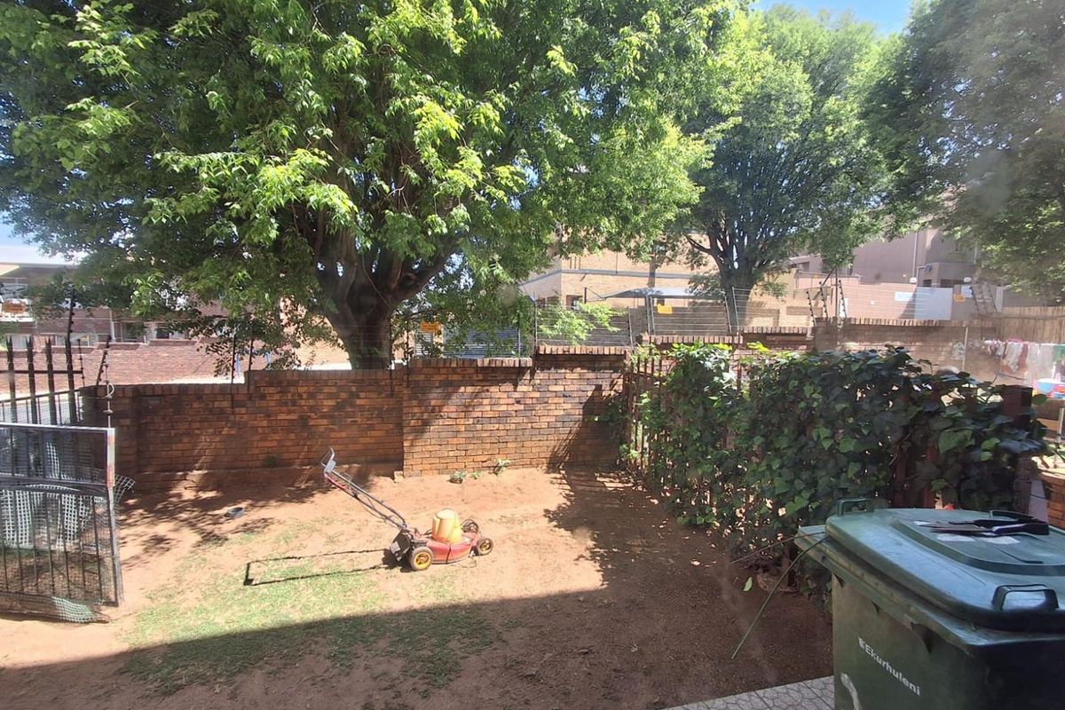 A private rear garden area featuring a brick boundary wall, mature trees, and paved patio space.