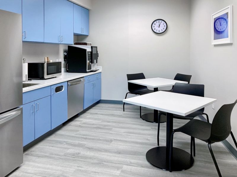 A clean and functional office kitchenette featuring light blue cabinetry, white countertops, integrated dishwasher, and durable vinyl plank flooring.