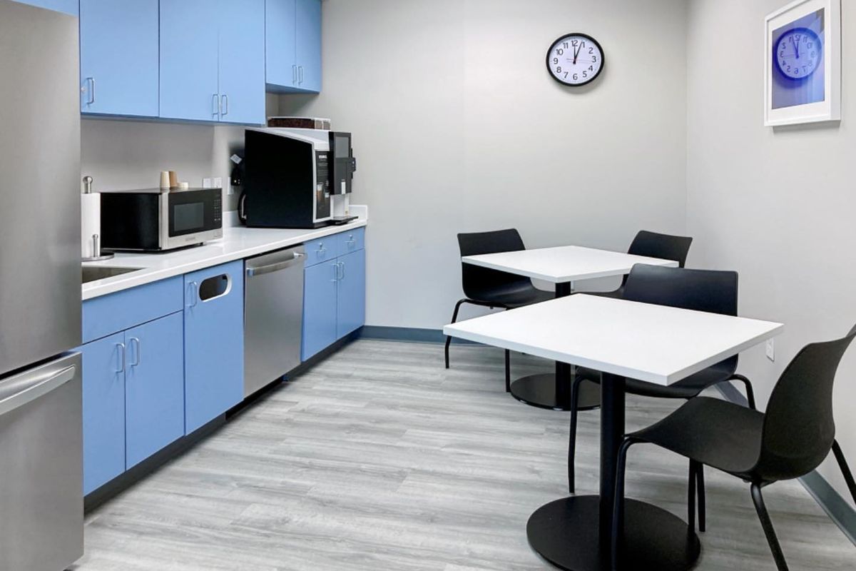 A clean and functional office kitchenette featuring light blue cabinetry, white countertops, integrated dishwasher, and durable vinyl plank flooring.