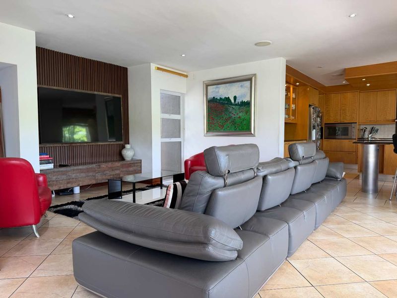 Spacious open-plan living area featuring a modern slatted wood feature wall, tiled flooring, and a functional kitchen with integrated cabinetry and breakfast bar.