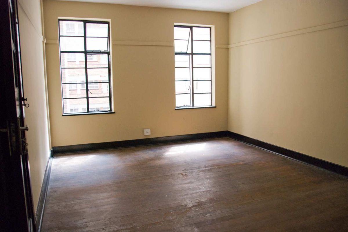 An empty bedroom featuring original hardwood flooring, steel-framed windows, and classic picture rails, offering a blank canvas for renovation.