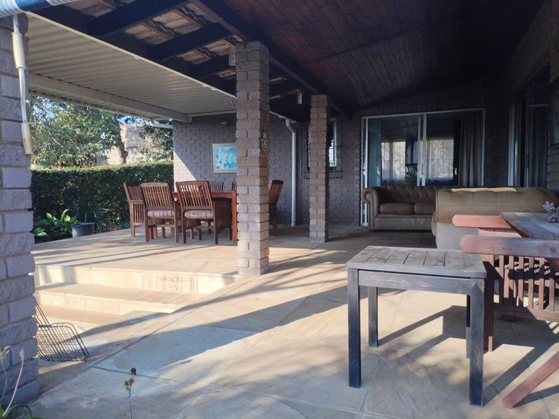 A spacious covered patio featuring brick columns, stone flooring, and a timber ceiling, providing a functional outdoor entertainment area with direct access to the home.