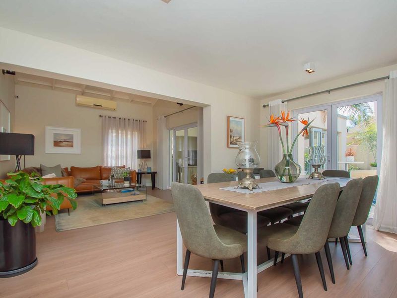 Spacious open-plan living and dining area featuring light laminate flooring, air conditioning, and large glass doors leading to the outdoor patio.