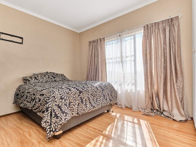 A standard bedroom featuring laminate flooring, neutral wall tones, and a large window with security bars and curtain tracks.