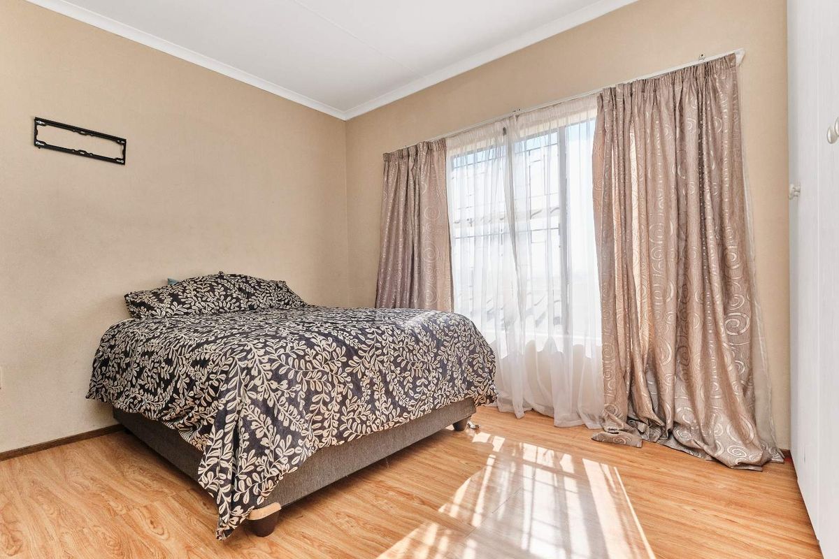 A standard bedroom featuring laminate flooring, neutral wall tones, and a large window with security bars and curtain tracks.