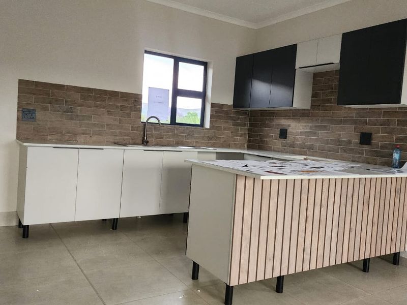 Modern kitchen featuring sleek white and black cabinetry, a wood-slat kitchen island, tiled backsplash, and neutral floor tiles in a clean, open space.
