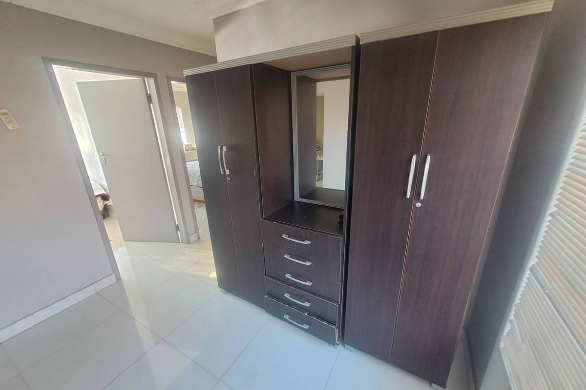 A bedroom featuring tiled flooring and dark wood built-in cupboards with an integrated vanity mirror.