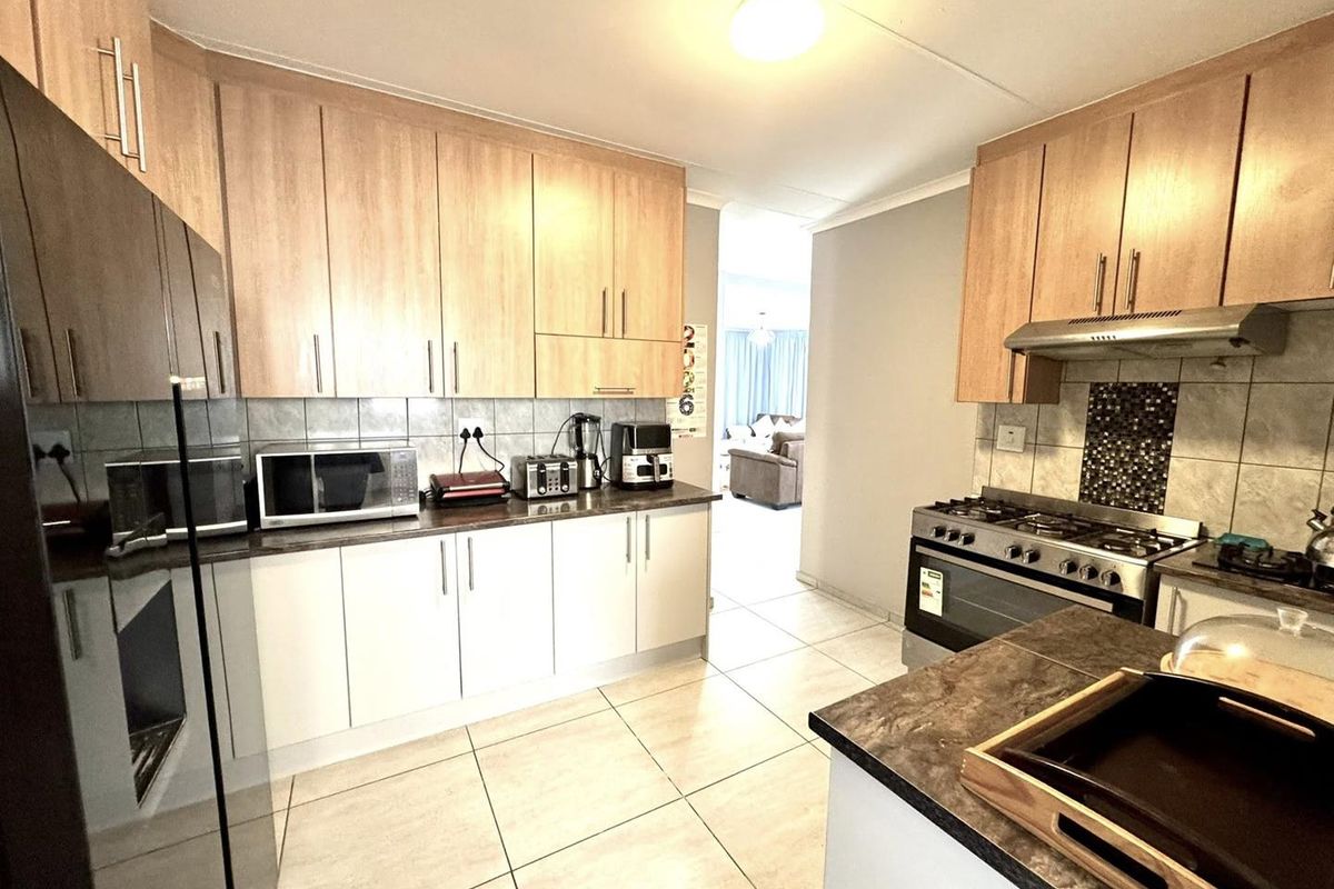 Functional kitchen featuring light wood cabinetry, stone-look laminate countertops, tiled flooring, and a stainless steel gas stove with extractor fan.
