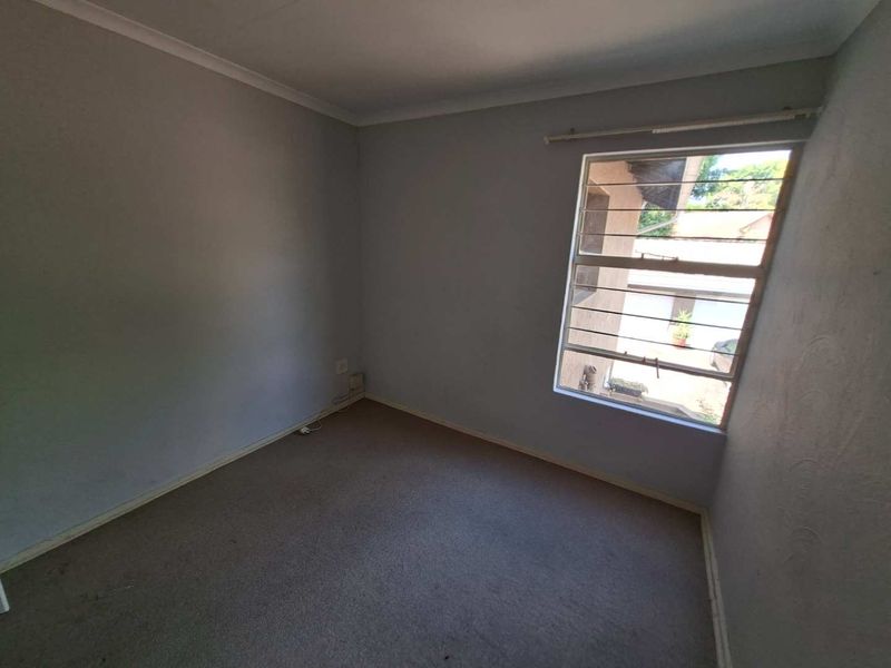 An empty bedroom featuring carpeted flooring, a window with security bars, and coved ceilings, offering a blank canvas for potential updates.