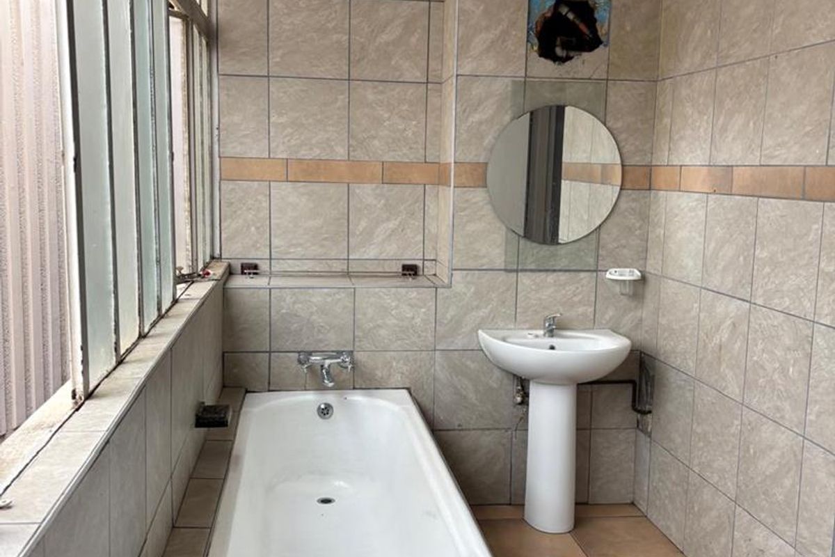 A dated bathroom featuring a built-in bathtub, pedestal basin, and tiled walls, requiring maintenance and cosmetic updates.