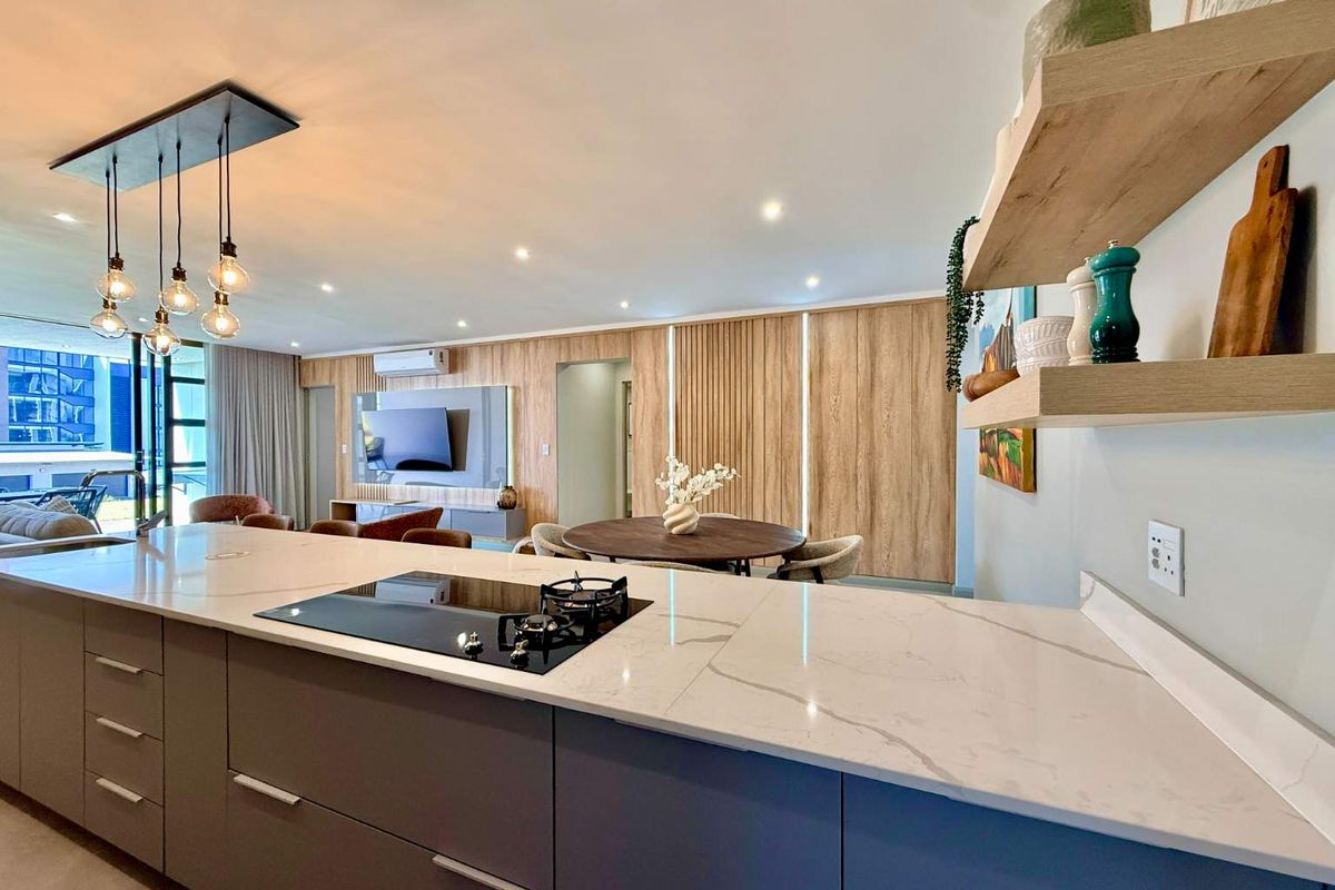 Modern open-plan living area featuring a sleek kitchen island with stone countertops, gas cooktop, and elegant timber wall paneling with integrated lighting.