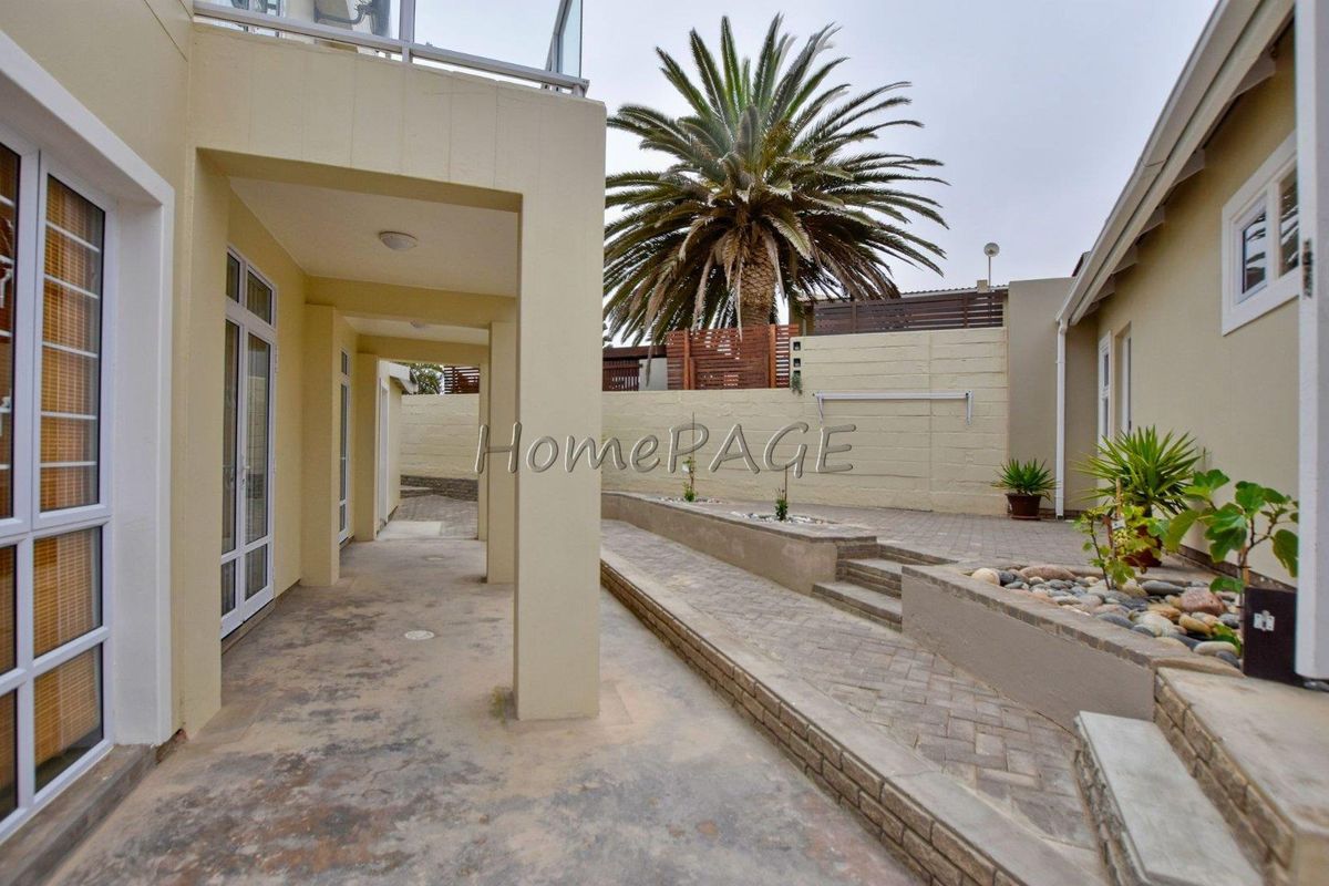 A paved rear courtyard area featuring a covered patio, tiered garden beds, and a perimeter boundary wall.