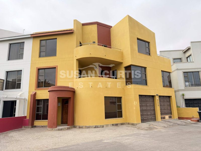 Three-story townhouse exterior featuring a double garage, balcony, and distinctive yellow and terracotta facade with paved driveway access.