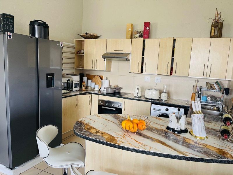 A functional kitchen featuring light wood cabinetry, stone-look breakfast bar, built-in oven, extractor fan, and integrated laundry appliance.