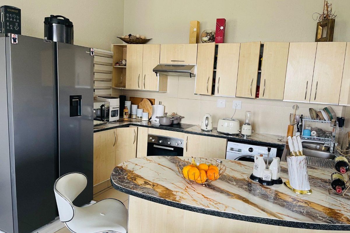A functional kitchen featuring light wood cabinetry, stone-look breakfast bar, built-in oven, extractor fan, and integrated laundry appliance.