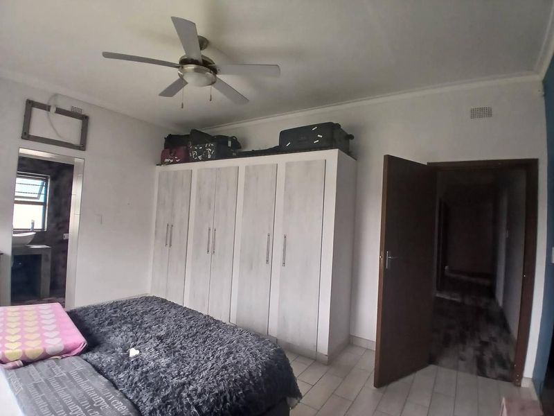 A bedroom featuring built-in wardrobes, tiled flooring, and a ceiling fan, with an adjacent en-suite bathroom visible through the doorway.